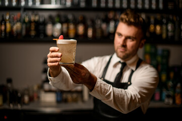 Old-fashioned glass with fresh foamy cocktail which barman holds in hands