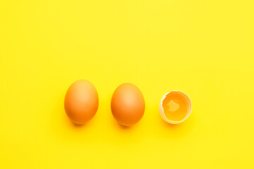 Cracked and whole chicken eggs on yellow background