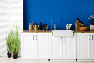 White counters with sink, food and kitchen utensils near blue wall