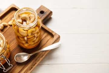 Jars of tasty cashew nuts with honey on white wooden background