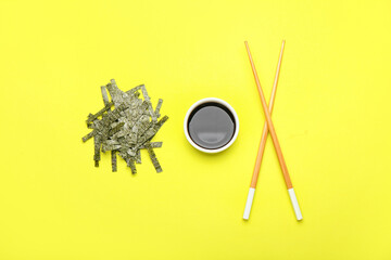 Chopped seaweed sheets, bowl with soy sauce and chopsticks on yellow background