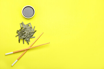 Chopped seaweed sheets, bowl with soy sauce and chopsticks on yellow background