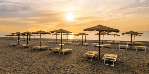  empty beach during beautiful sunrise or sunset with chaise loungues and nice umbrellas with blue...