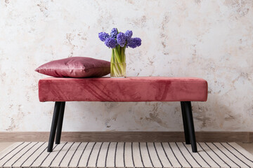 Vase with hyacinth flowers and pillow on bench near light wall in room
