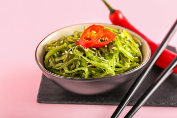 Bowl with healthy seaweed salad and chili pepper on pink background