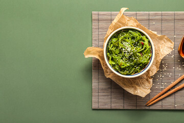 Bowl with healthy seaweed salad on green background