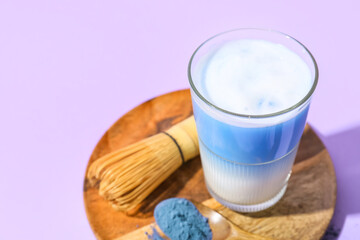 Glass of blue matcha tea, chasen and spoon with powder on purple background