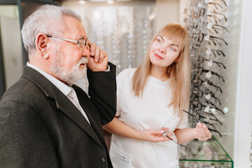 an elderly man with an ophthalmologist chooses glasses in the optics salon.