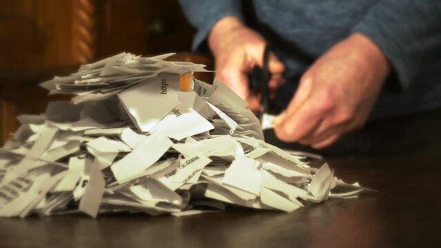 A rack focus / differential focus closeup of a man in the background, using scissors to cut up important papers, blurring as focus switches to a pile of shredded documents in the foreground.