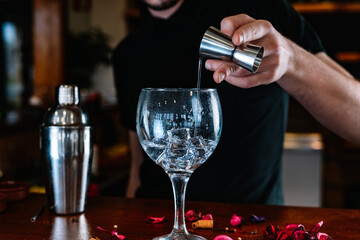 detail of hands bartender pouring liquor into a crystal glass to prepare a mixed drink at the bar counter.
