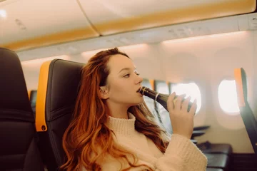 Foto op Plexiglas The girl in the plane drinks champagne alcohol from excitement. Fear of flying on an airplane. © MoreThanProd