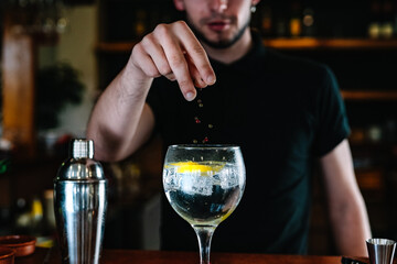 Detail of a bartender's hands adding ingredients into a crystal glass with ice for mixed drinks. Nightclub.