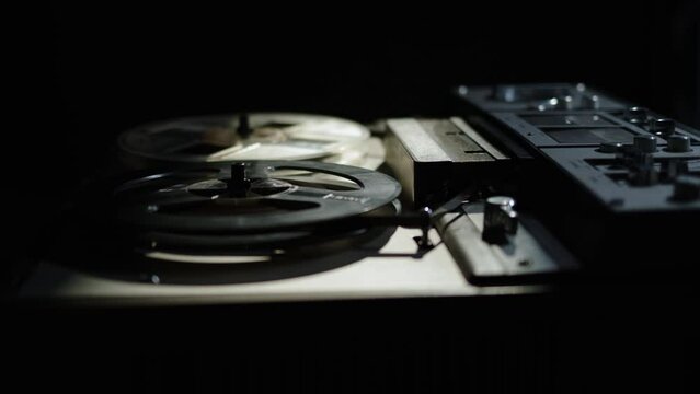 Rack focus close up old reel-to-reel tape recorder plays magnetic tape record. Beautiful gloomy shot of vintage retro turntable on table dark light. beam of light falls on old reel player.