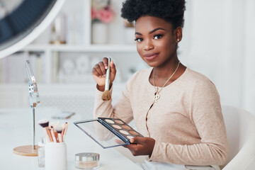 Beautiful African American Woman applying her makeup on with professional cosmetics products at home