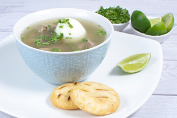 Chicken consomme, traditional Colombian food, accompanied by hard-boiled egg, corn arepas, cilantro...