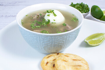 Chicken consomme, traditional Colombian food, accompanied by hard-boiled egg, corn arepas, cilantro and lemon