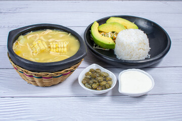Ajiaco, traditional Colombian food, accompanied by rice, milk cream, avocado, capers and salad