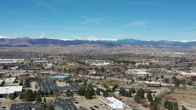Aerial view of Longmont, Colorado with front range mountains in the distance. Drone footage of suburban sprawl with retail stores and shopping plazas.