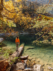Traveller woman on wooden log at crystal mountain lake in the autumnal landscape.