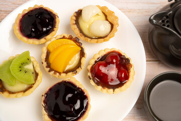 Homemade Fruits tarts, Sweet desserts topping with fresh kiwi, blueberries, peach, longan, raspberries in syrup, served with hot herbal tea on wooden table	
