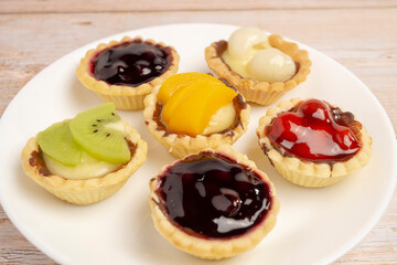 Homemade Fruits tarts, Sweet desserts topping with fresh kiwi, blueberries, peach, longan, raspberries in syrup, on wooden table.	
