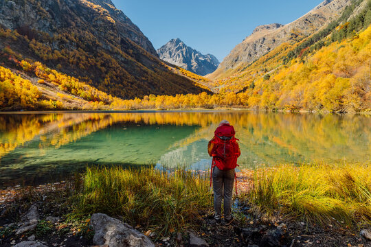 Hiker woman at lake in autumnal mountains. Mountain lake and tourist with backpack