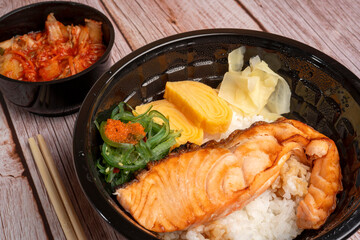 Japanese meal in a Bowl on the wooden table background - rice bowl topped with grilled salmon, sweet egg roll and seaweeds salad.	

