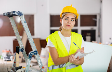 Woman foreman in a protective helmet and yellow vest checks the completed construction work on the...