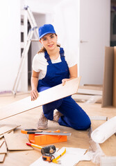 Caucasian woman construction worker setting wooden laminate board on floor.