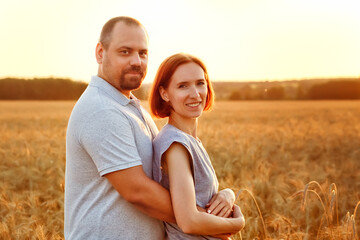 Portrait of a happy man and woman on the background of a ripe field with wheat. A couple in love, embracing on a sunny day. In the summer on a wheat field