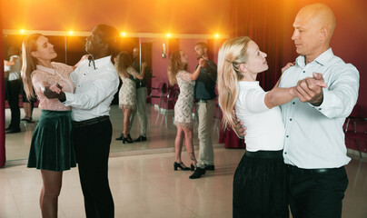 Young positive people learning to dance waltz together in dancing class