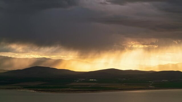 Sun rays beaming light through rainstorm moving over the farmland by Utah Lake during Spring thunderstorm.