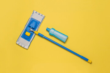 Cleaning agent and a mop on a yellow background. The concept of maintaining cleanliness. Flat lay.