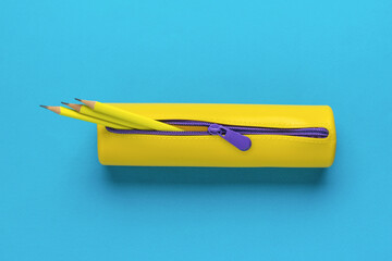 Yellow pencil case with three yellow pencils on a blue background. Flat lay.