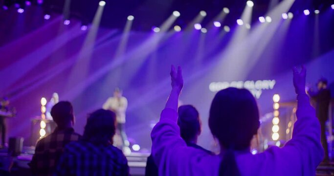 Female Christian Worships and Praises God on Music Concert, Youth Festival or Conference. Christian Believers Sing Songs with Raised Hands on Live Stage Event. 4K backside view handheld shot
