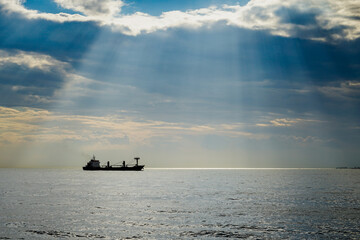 A beautiful view of a boat on the sea and sun rays between the clouds 