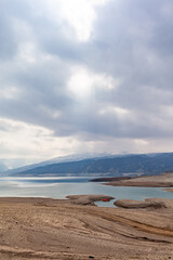 A beautiful reservoir in the mountains. Low water level, drought and beautiful patterns are visible along the banks. A red pleasure boat is standing by the shore