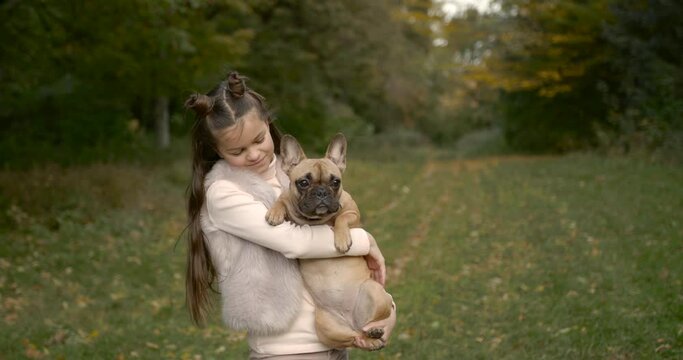 Girl with long hair holding a French bulldog in her arms