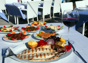 Grilled perch fish (Turkish: Levrek) with appetizer foods and red wine on the dinner plate.