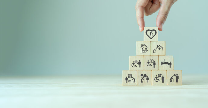 Elderly Care Concept. Hand Holds Wooden Cubes With Icons Related To Elderly Care, Medical, Rehabilitation Service, Nursing Care For Enhancing Quality Of Life In Elder Age. Used For Banner, Background.