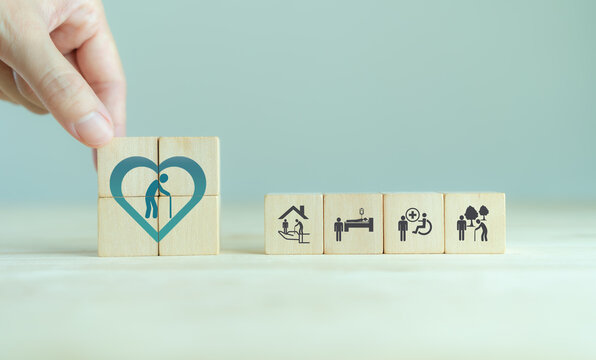 Elderly care concept. Hand holds wooden cubes with icons related to elderly care, medical, rehabilitation service, nursing care for enhancing quality of life in elder age. Used for banner, background