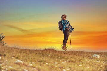 A woman hiking with a backpack and poles at sunset. Selective focus