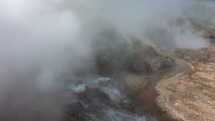 The eruption of a geyser. Water boils in a stone cauldron on the hillside. There are splashes and thick steam in the air. A river flows from hot springs in the valley. Kamchatka. Valley of Geysers