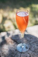 orange wine cocktail drink sitting outdoors on wood stump with green bokeh background