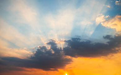 Blue and orange sunset sky with rays of sun. Sun rays slipping through clouds while sun sets.
