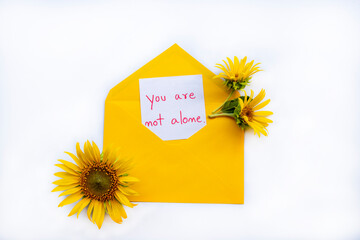 you are not alone message card handwriting in envelope with yellow flowers sunflowers arrangement flat lay postcard style on background white 