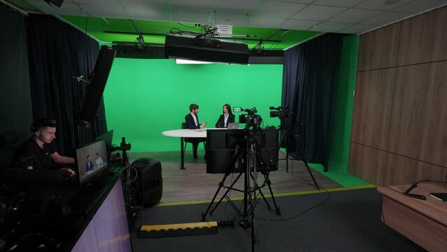 TV presenters, journalist interview a businesswoman, view of a backstage studio TV news shooting, chroma key template.
