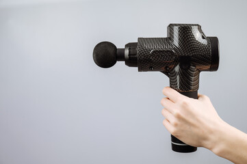 Close-up of a female hand with a portable massager gun on a white background. 