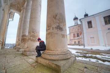 The boy is sitting near the column of an old building of the 18th century.