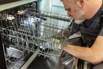 Portrait Of Male Technician Repairing Dishwasher In Kitchen